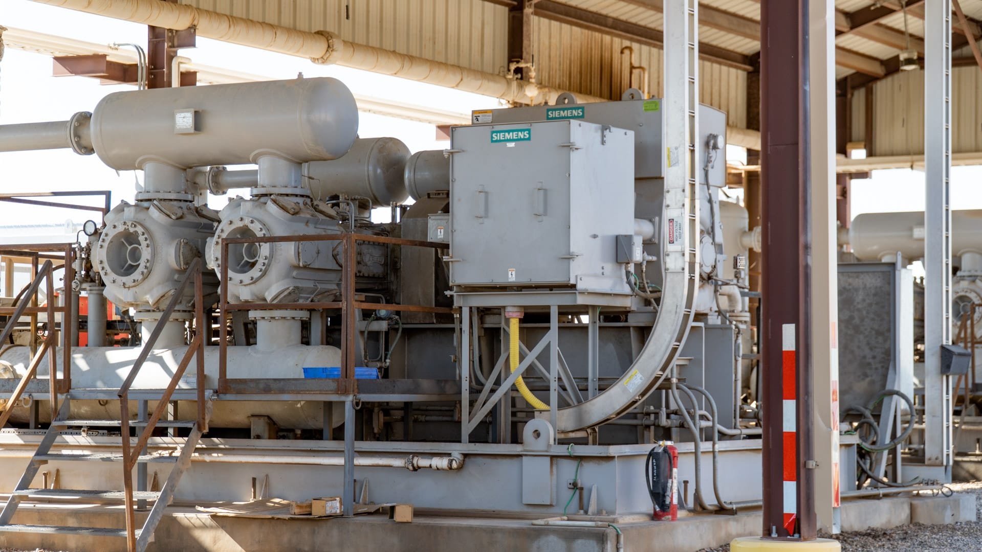 Two gas compressor packages and coolers beneath a steel shade structure on a gravel pad